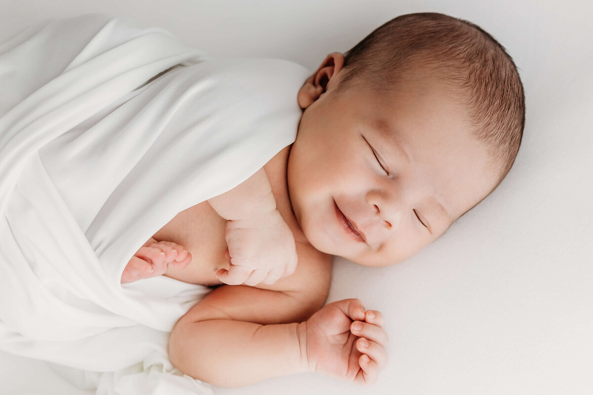 Smiling sleepy baby in white wrap in studio near Eau Claire, WI