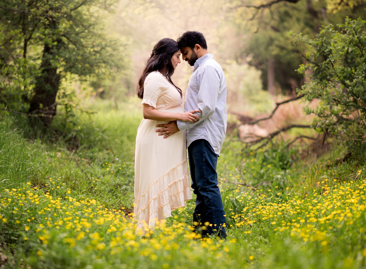 Pregnant couple standing in a field of yellow flowers