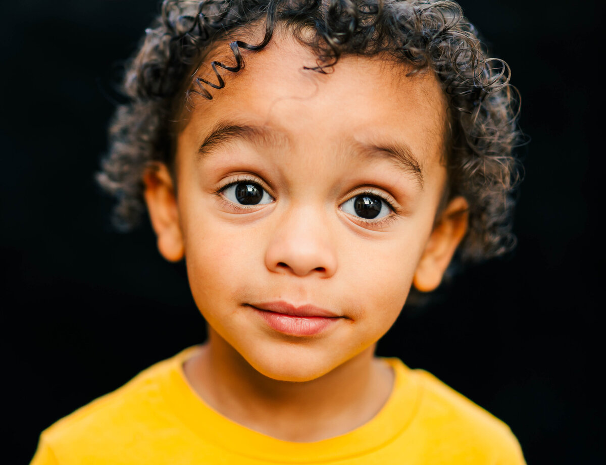 fine art portrait of toddler boy in profile with black backdrop and moody tones