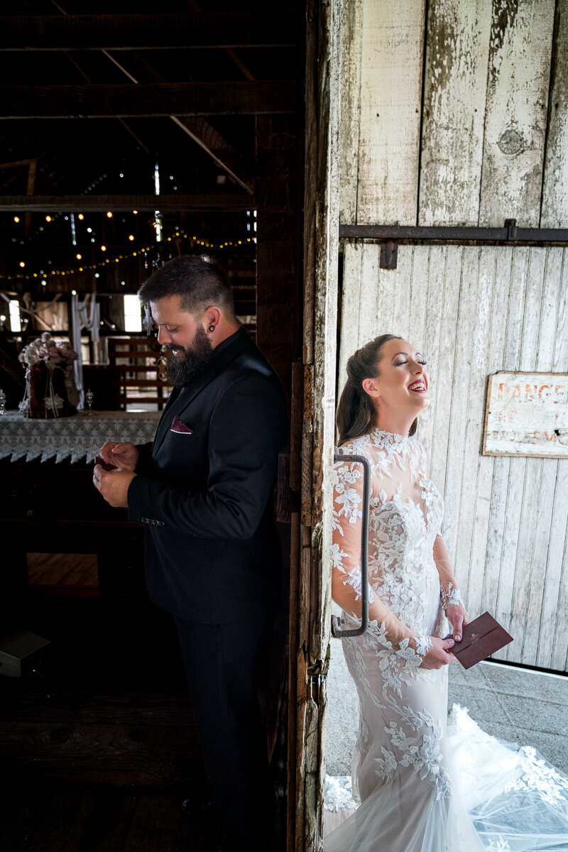 A touching and joyful moment as the bride and groom read notes and laugh while standing on opposite sides of a barn door after their first touch at North Coast Hitching Post in Humboldt, CA, capturing the anticipation and love before their ceremony.