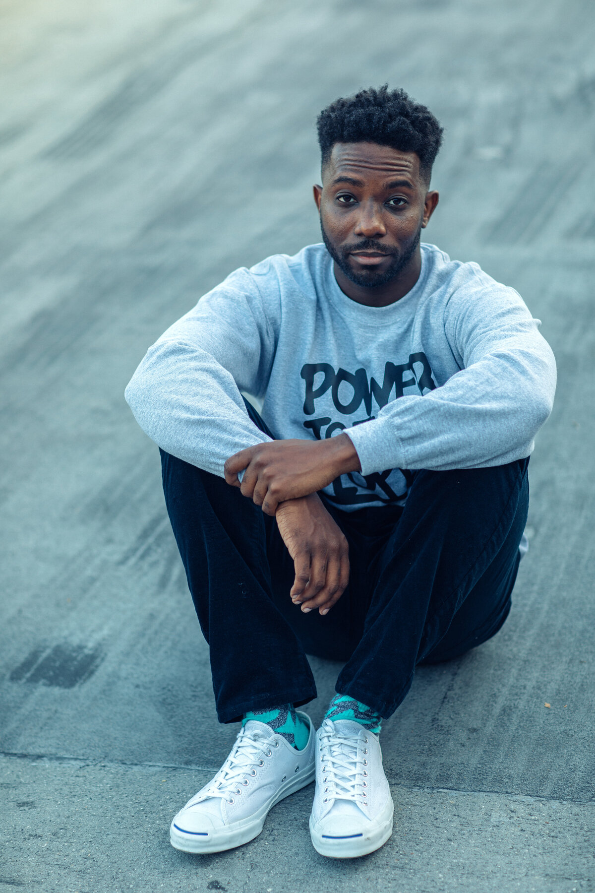 Portrait Photo Of Young Black Man Sitting With Both Arms On Top Of His Knees Los Angeles