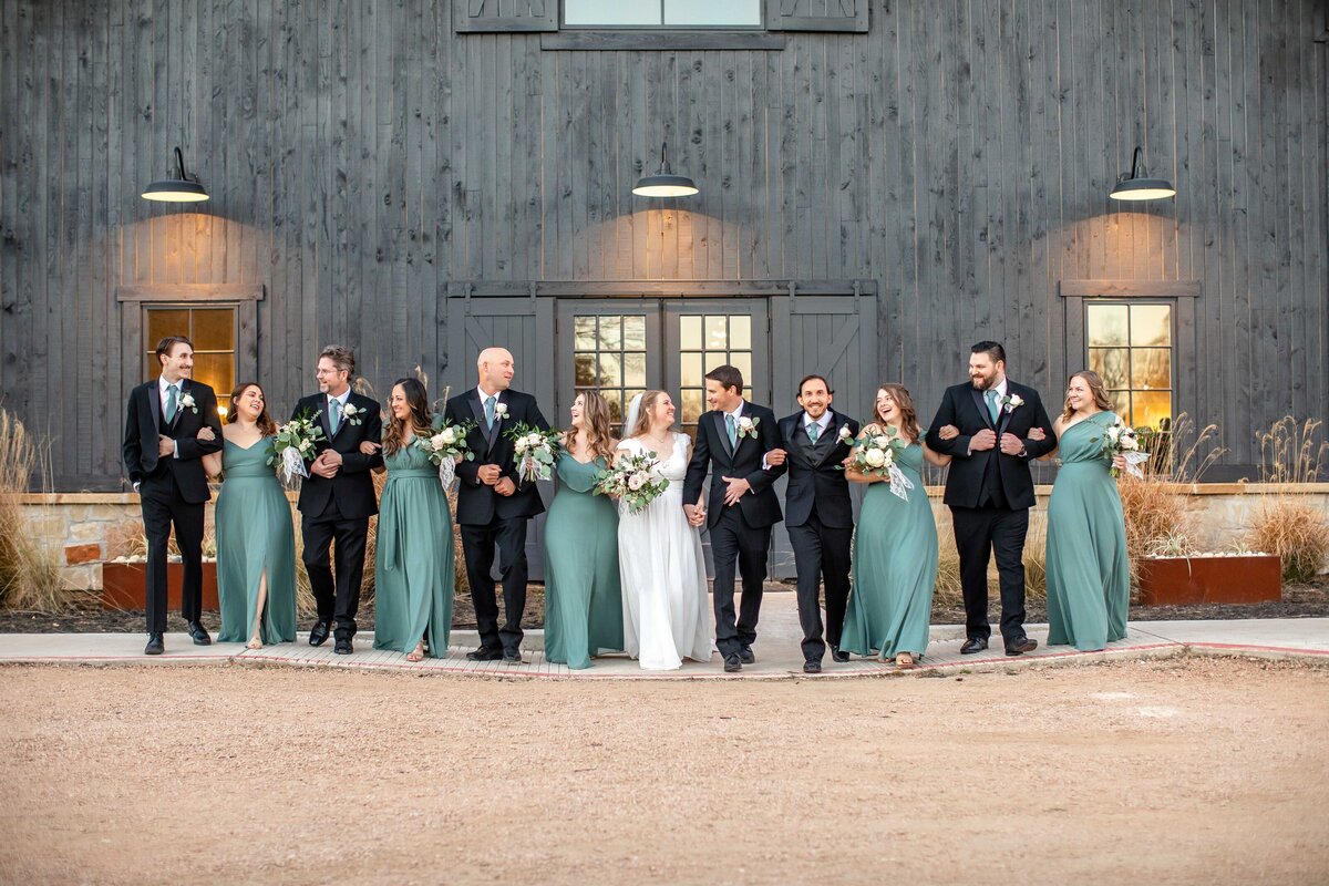 wedding party of 10 join arm in arm with bride and groom  at Morgan Creek Barn  in Dripping Springs