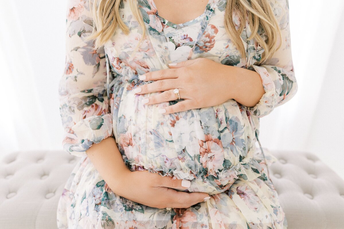 maternity photo of pregnant mom holding her baby bump wearing a floral dress for studio photos