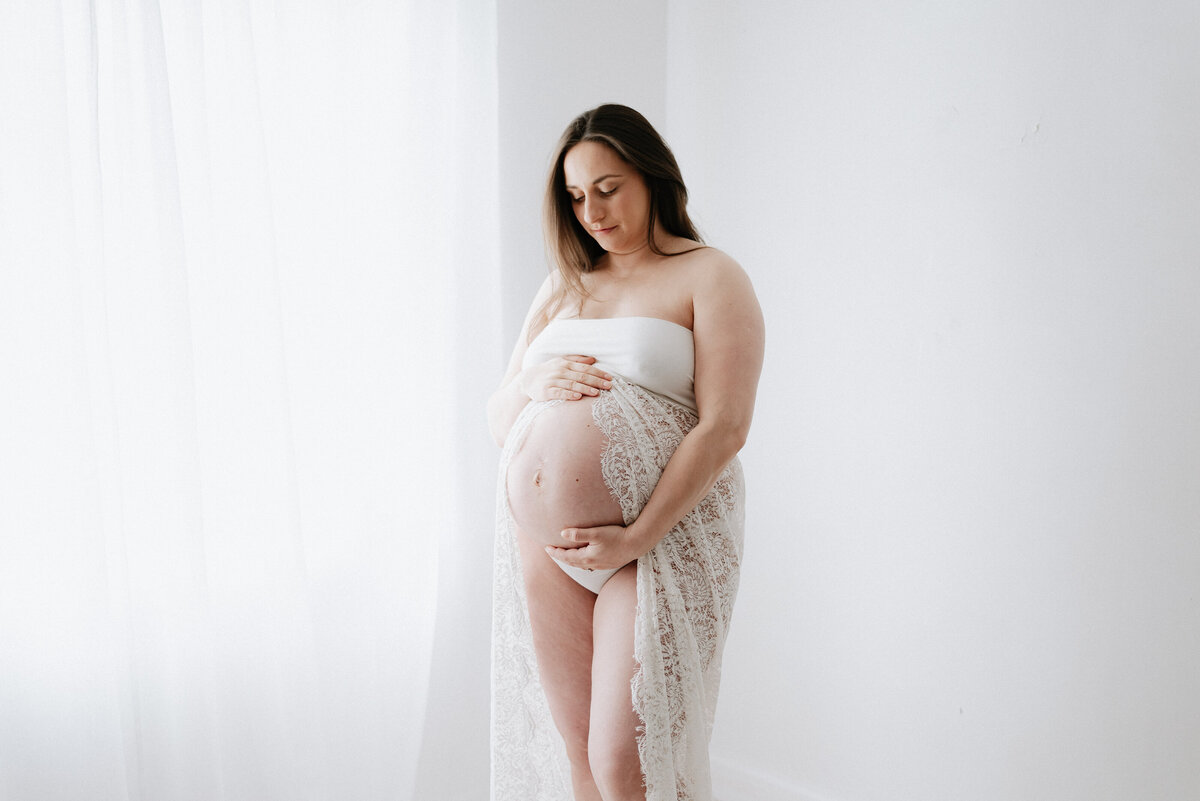 A women standing in an all white studio in billingshurst maternity photoshoot