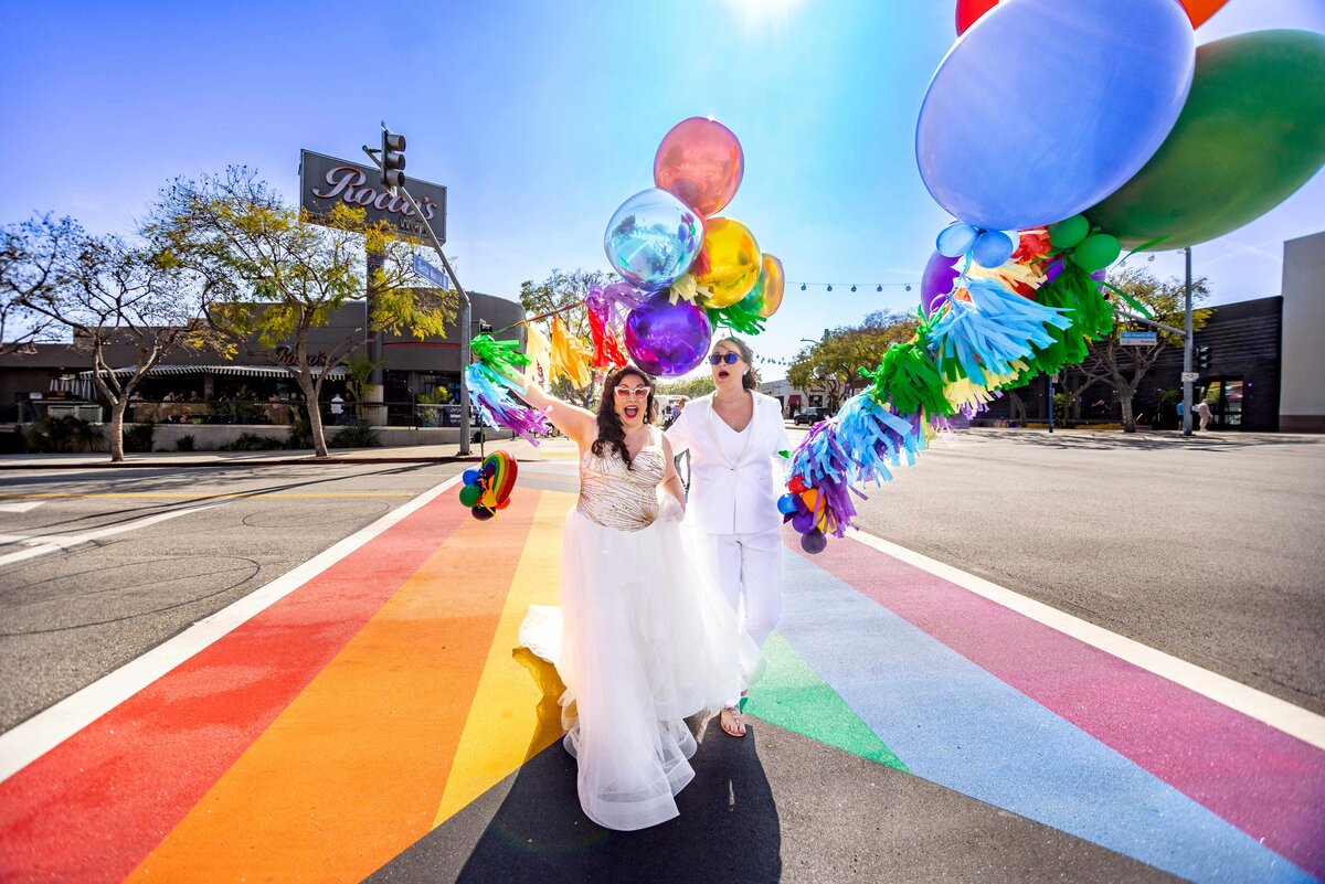 Two brides smiling and walking across a painted crosswalk.