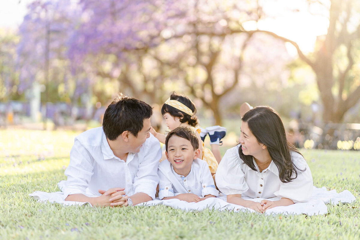 family lying on the grass soaking up sunset light in jacarandas during family photo session in brisbane