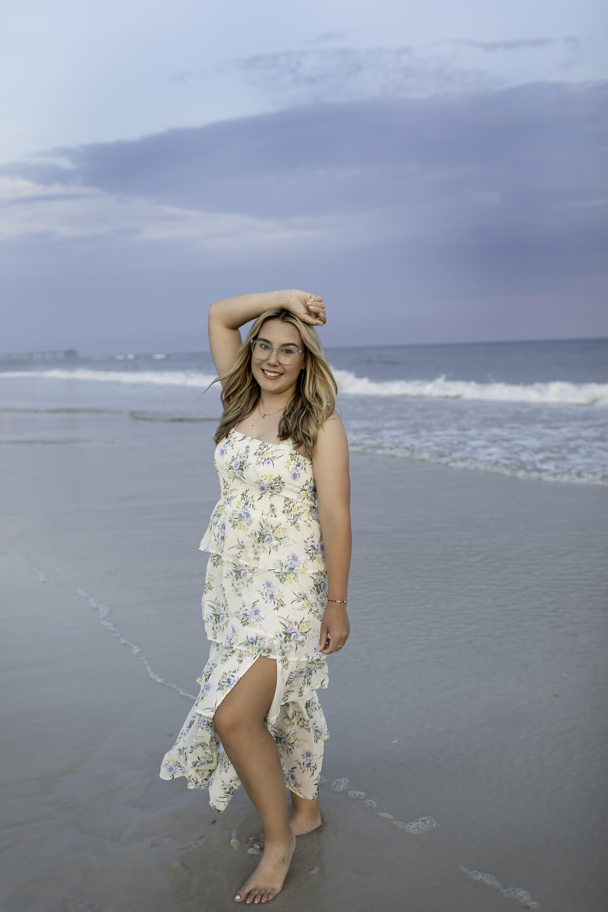 A serene senior photoshoot at the beach, with the graduate standing on the shoreline, feeling the sand between their toes as they reflect on their journey