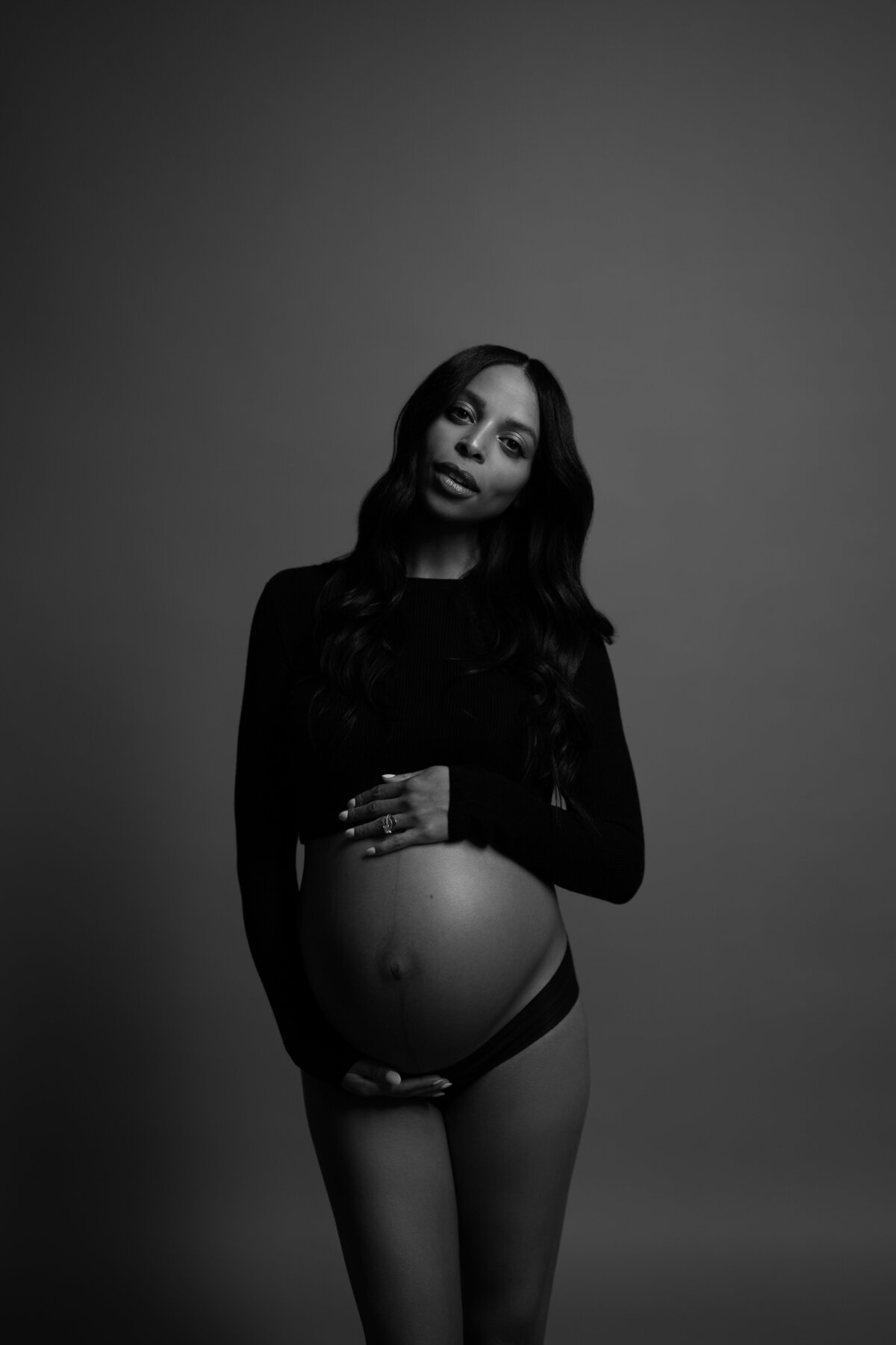 A timeless black-and-white maternity photo showcasing a serene expression and hand resting on the baby bump, taken in a studio in NYC.