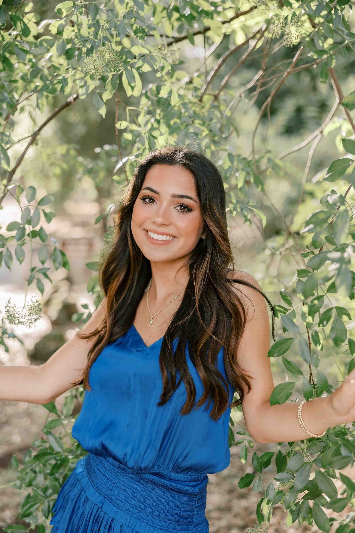 Brunette girl wearing a royal blue dress and peeking through an oak tree's branches