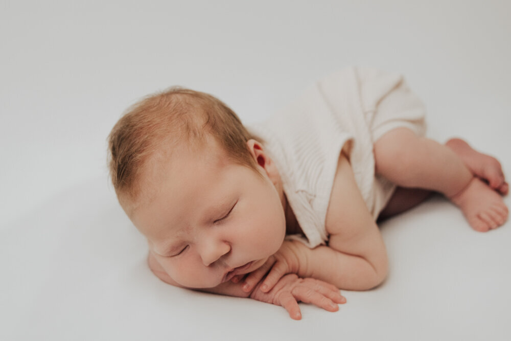 posed newborn baby lying on white blanket with chin on hands - Townsville Newborn Photography by Jamie Simmons