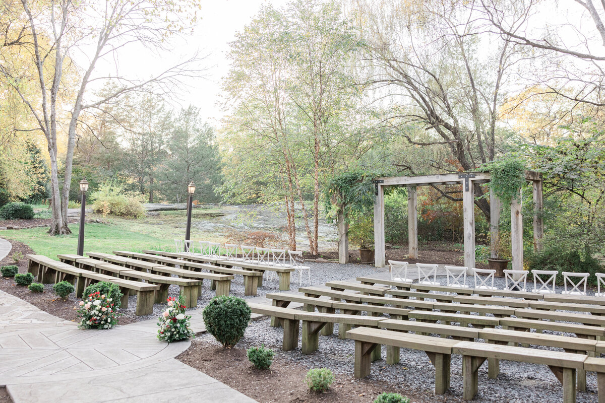 A wedding ceremony site with wooden benches along the aisle