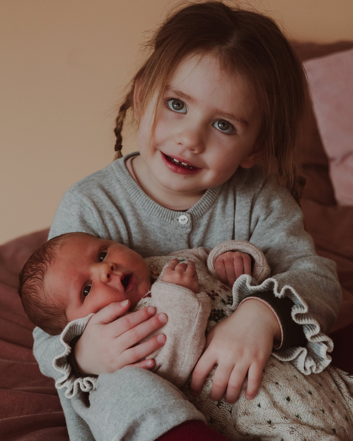 Een klein meisje houdt haar babyzusje vast met een liefdevolle glimlach op haar gezicht.