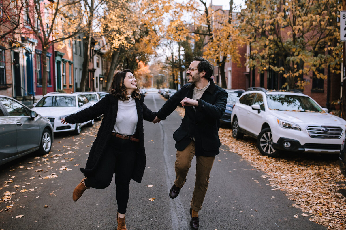 Engaged couple skipping through the Mexican War Streets of Pittsburgh during the fall.