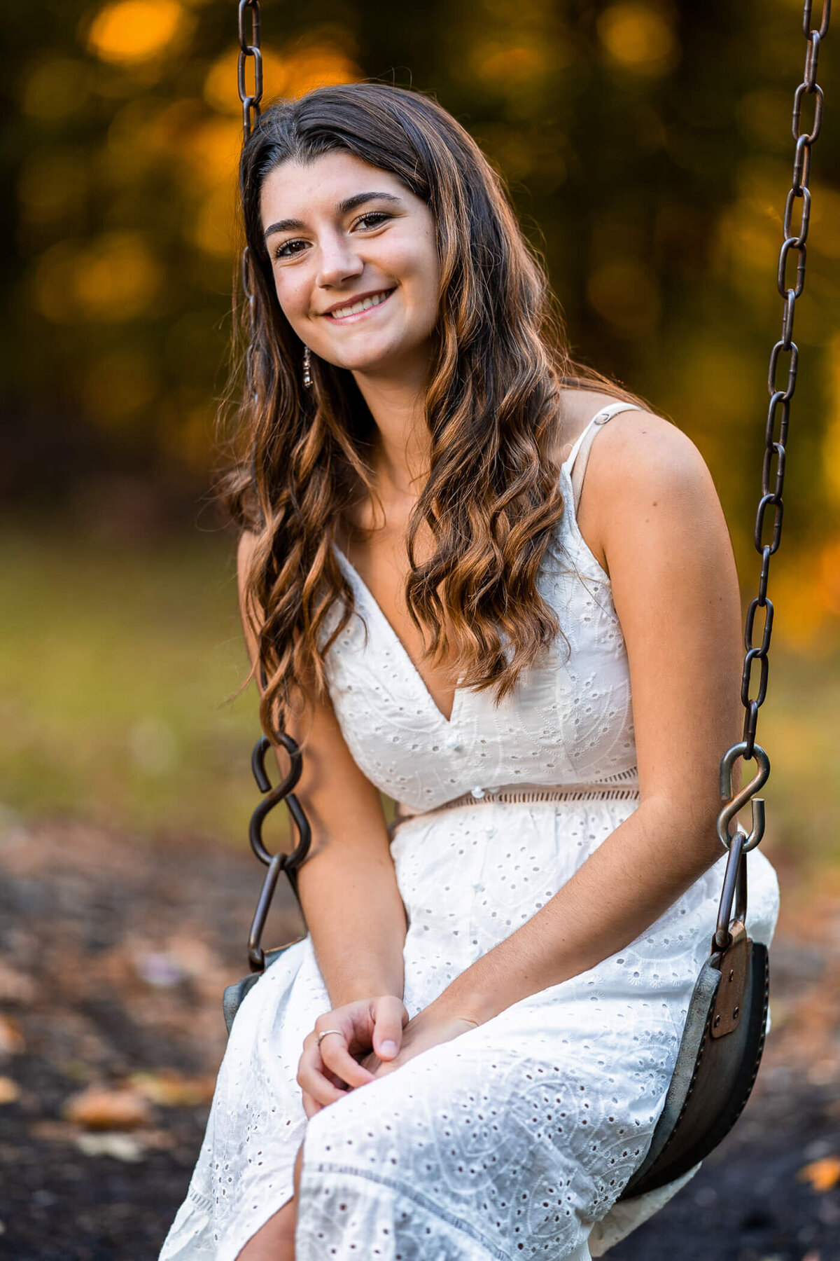 Senior portrait photography of a senior sitting on a swing set and smiling surrounded by autumn leaves