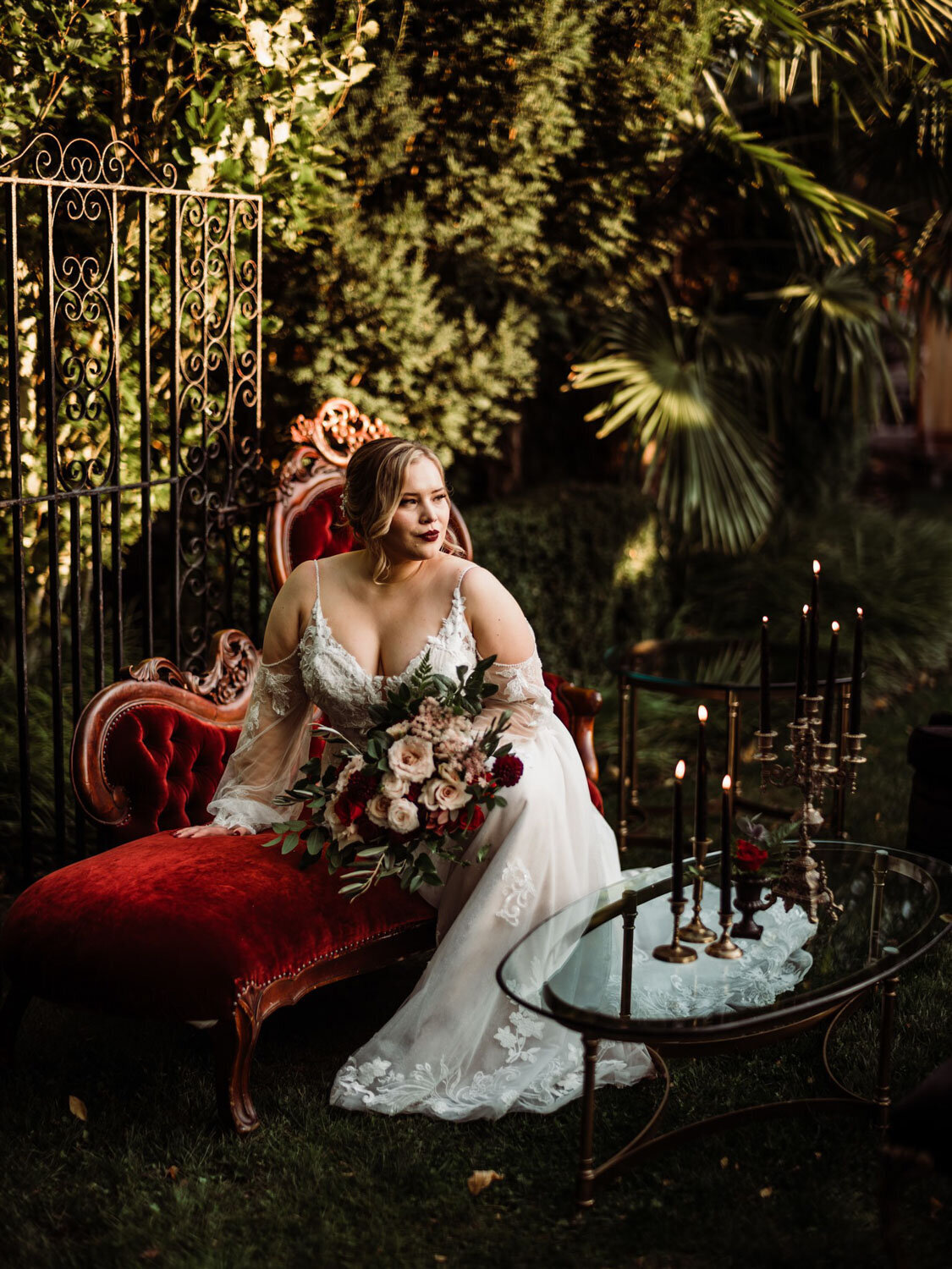 Bride seated on a vintage red chaise lounge with a bouquet