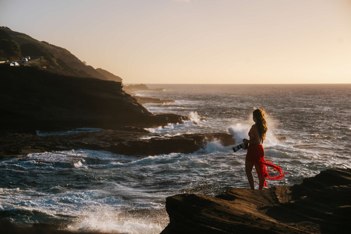 Woman holding camera with a view of crashing waves