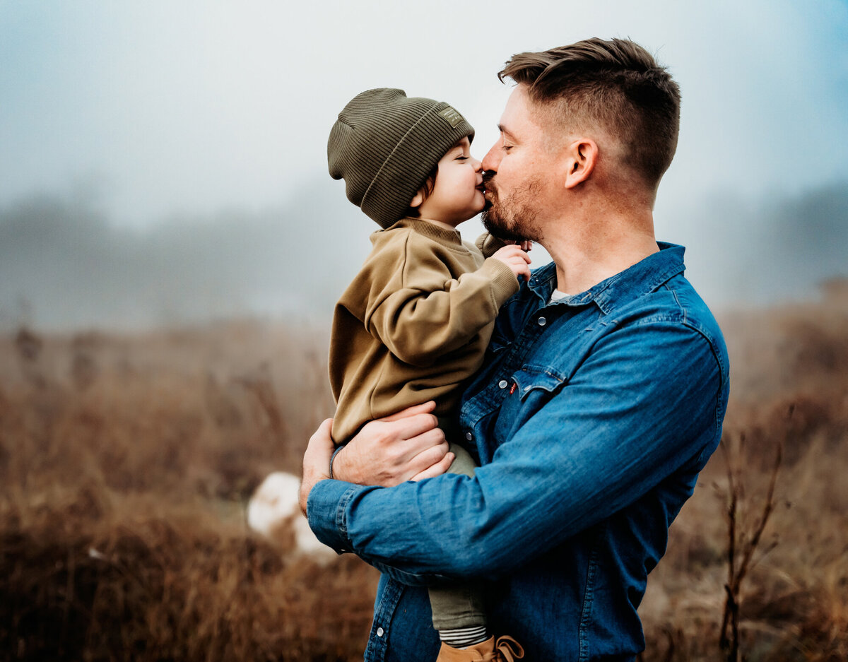 Family Photographer, a father gives his son a kiss as he holds him outside