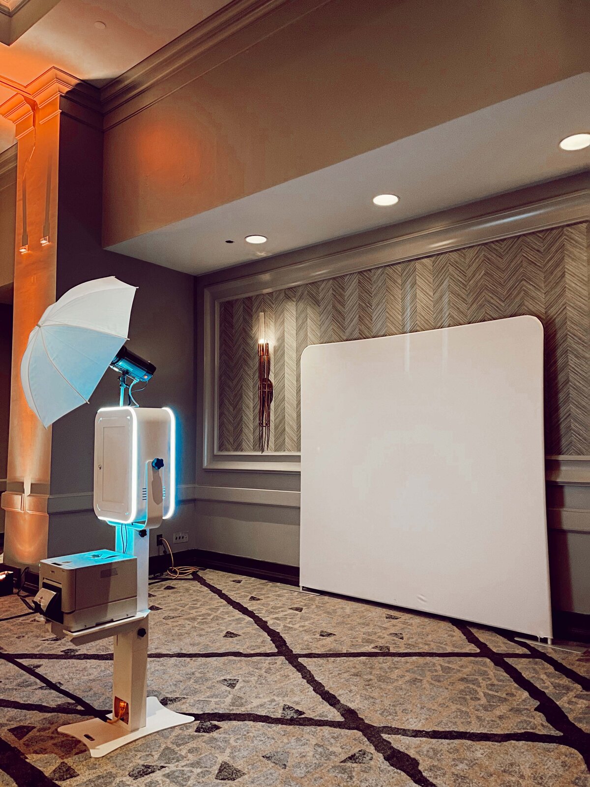Minimal white photo booth and white backdrop setup in a modern indoor space with warm lighting.