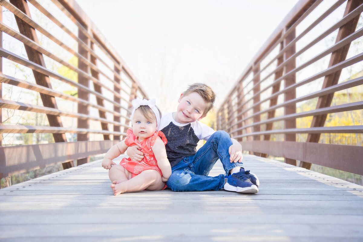 brother and sister sitting on a bridge smiling during a session with Las vegas milestone photographer Jessica Bowles