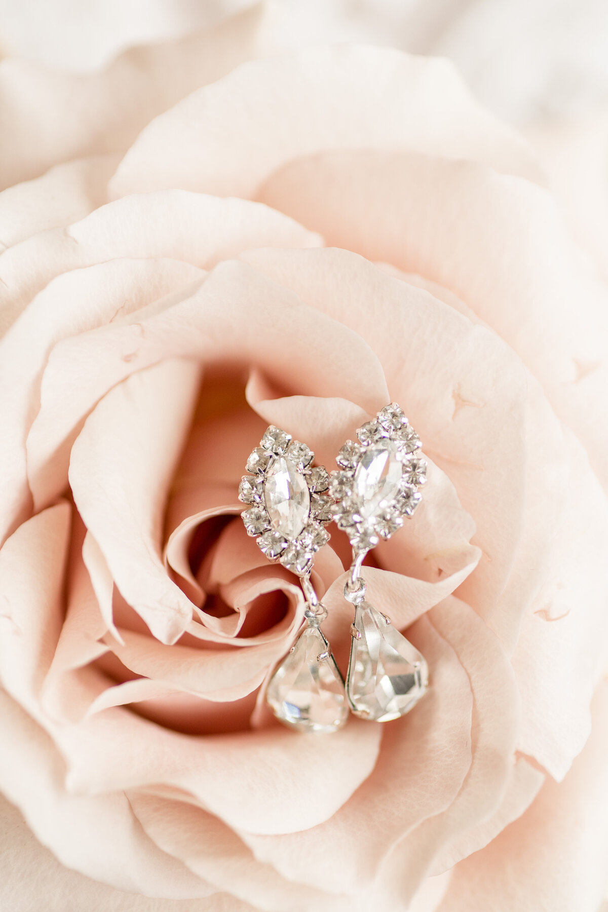 Beautiful dangly diamond earrings resting inside pale pink rose bud.