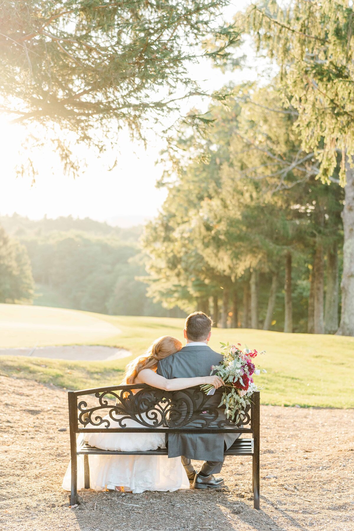 Bride and groom embrace while sitting on a bench during golden hour 