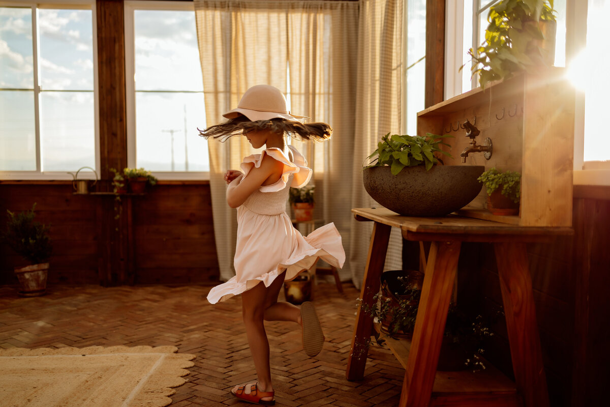 Young girl spins in her dress while the sun lays on her in a greenhouse while tending to plants for this Denver family photo session