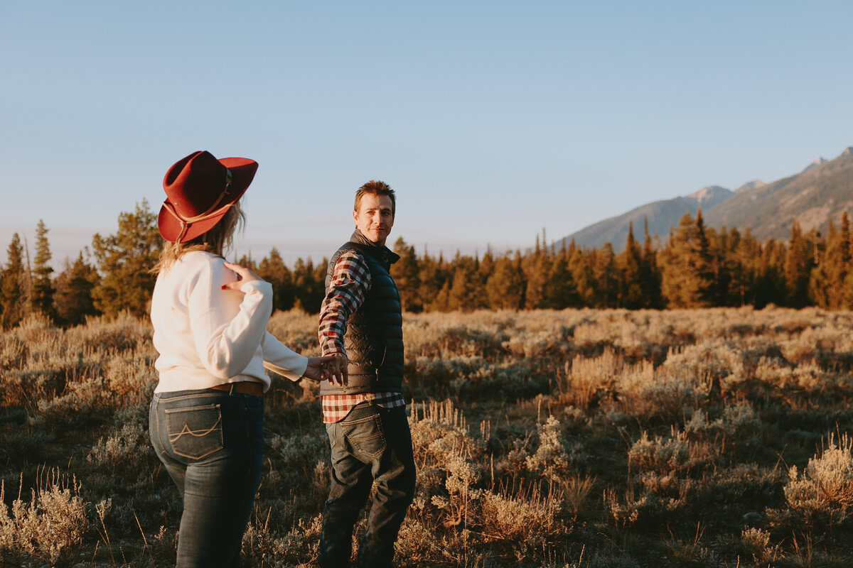 Photo of men holding womans hand walking during sunrise during Wyoming engagement session