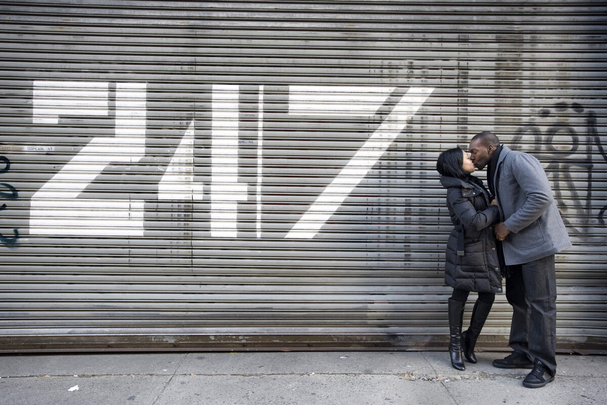 A couple kissing in front of an industrial garage door 