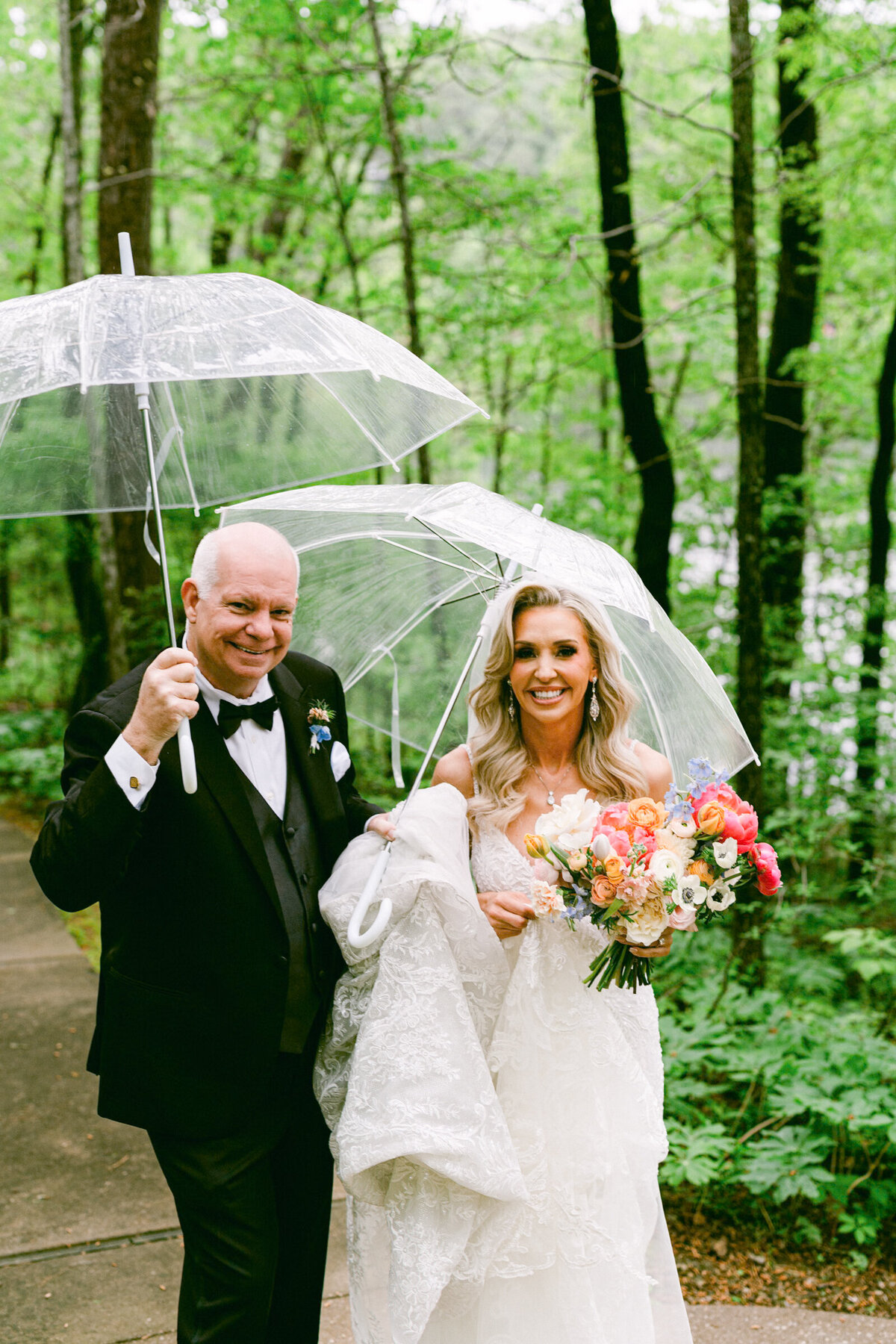 A wedding day photo of the bride and her father under umbrellas at Mildred B Cooper Chapel in Betonville Arkansas
