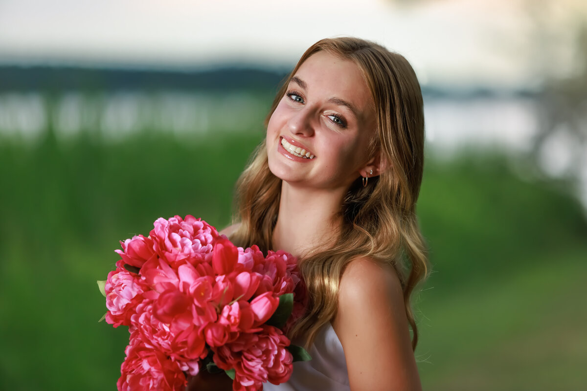 Teen Portraits in Holly Springs at sunset near a lake holding pink flowers.