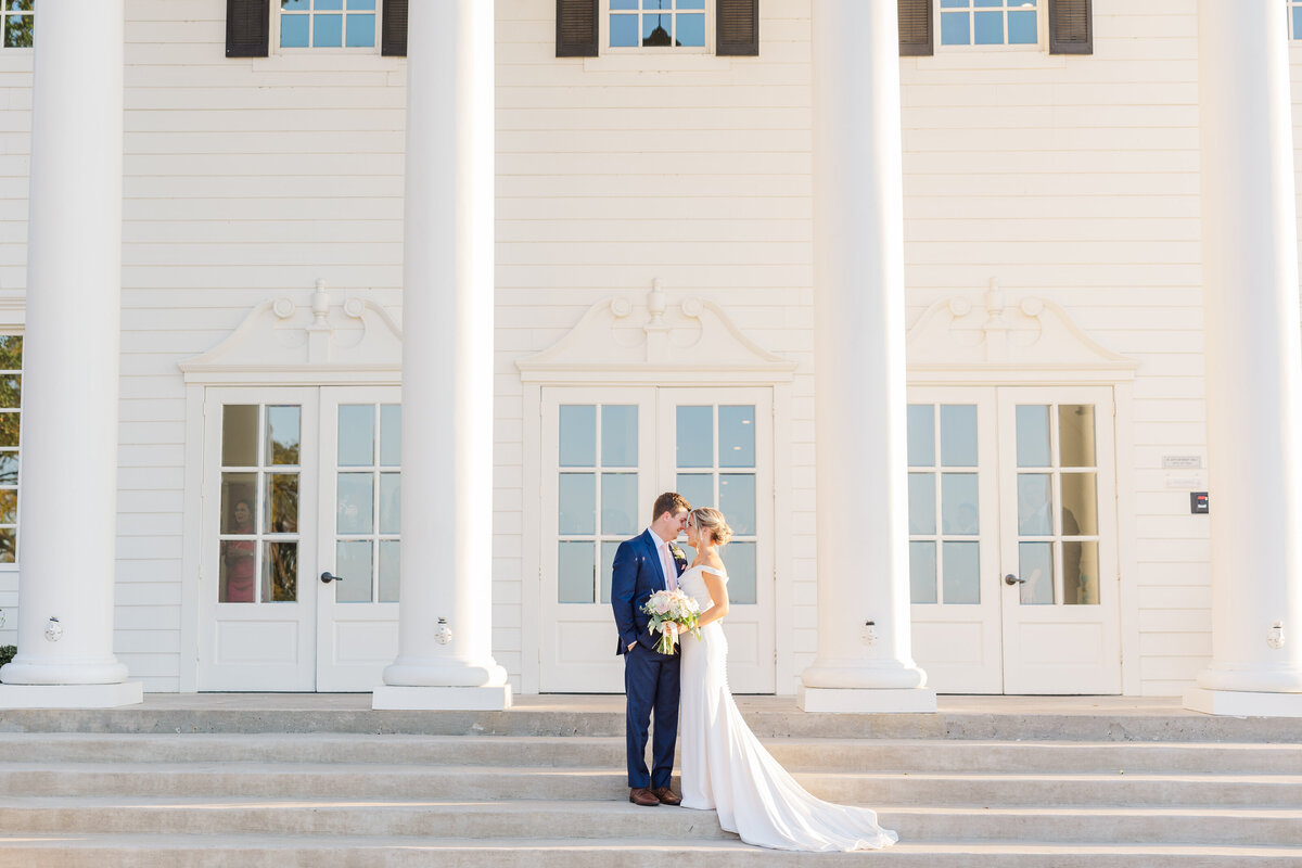 A light-filled wedding moment captured on the grand white steps of a stately venue, where the bride and groom share a quiet embrace beneath soaring columns. A dreamy, editorial-style image for couples looking for elegant and light and airy wedding photography near Coppell, Frisco, or Flower Mound.