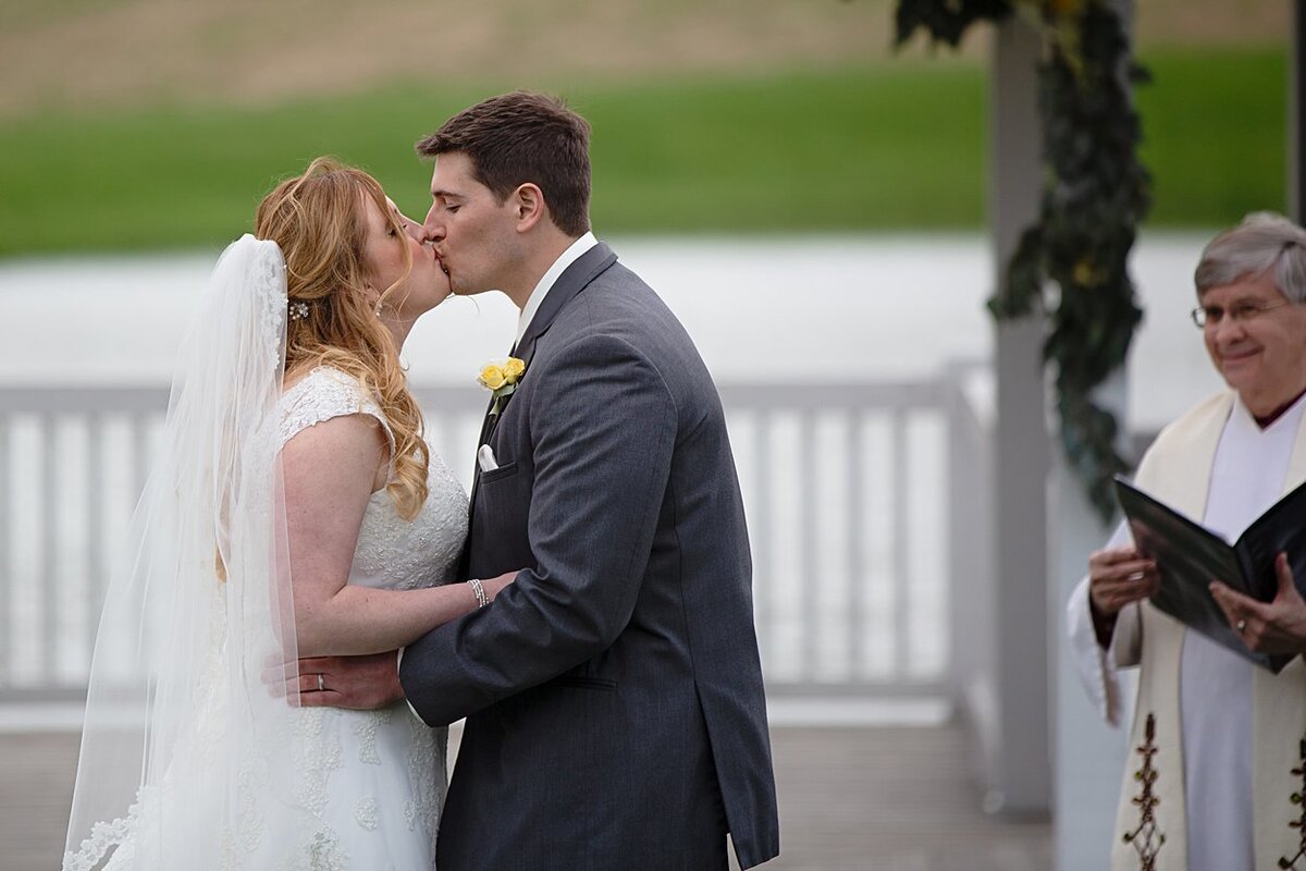 Bride and Groom share a first kiss during outdoor, lakeside wedding ceremony at White Barn in Prospect, PA