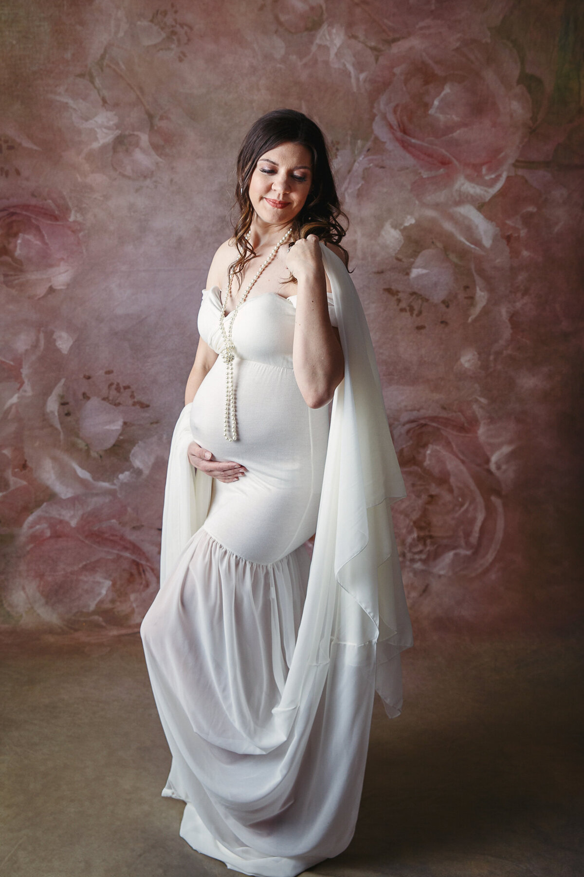 Pregnant woman in white maternity gown looking  down at her shoulder