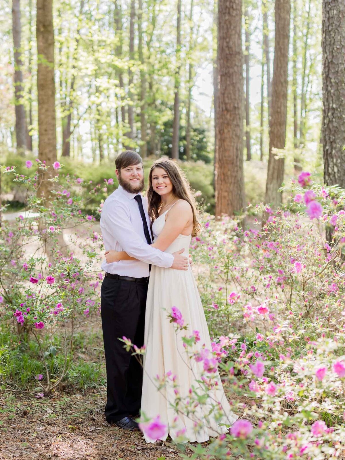 Engagement portrait of a couple wearing a white dress and suit  in the forest with flowers.