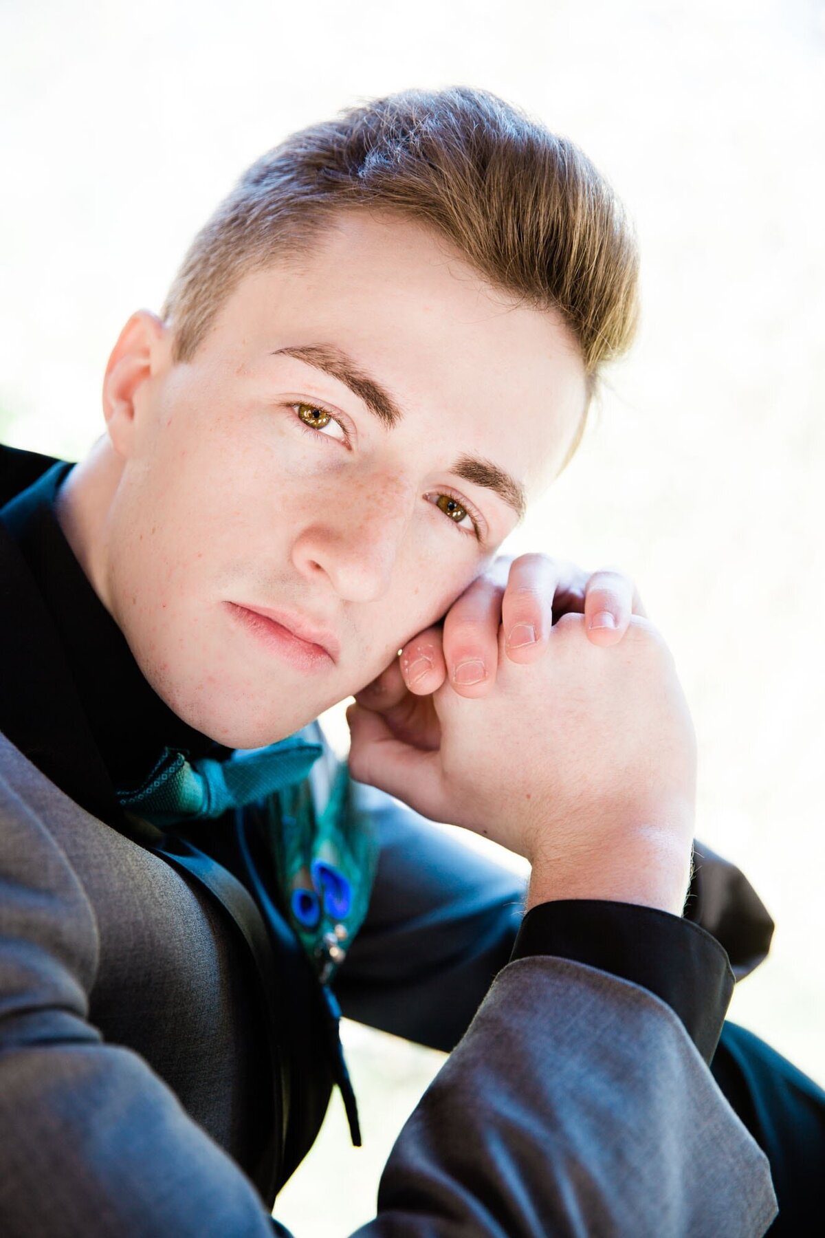 Boy posing with his hands against his face wearing a tuxedo for his senior prom.
