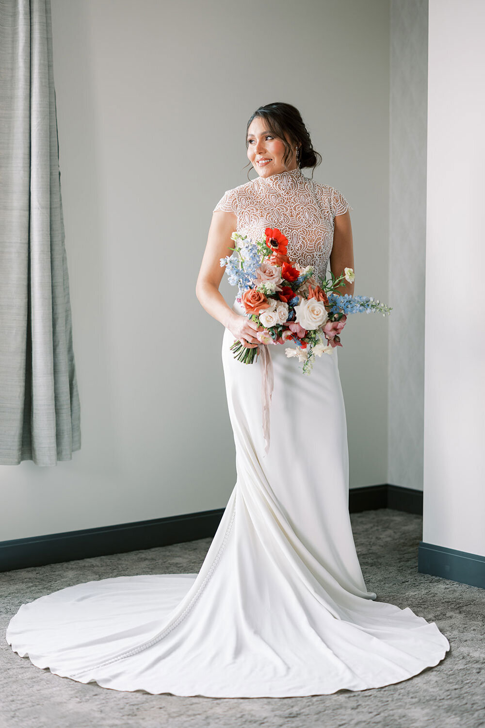 Bride in a high-neck lace wedding gown holding a colorful bouquet of roses, delphinium, and poppies, at the Kimpton Armory in Bozeman for a modern wedding inspiration shoot.
