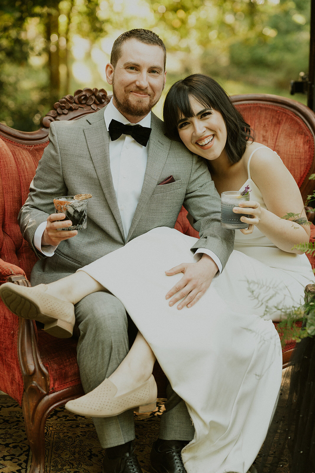 the-bride-and-the-groom-sit-on-the-sofa-with-glasses-in-hand-smiling
