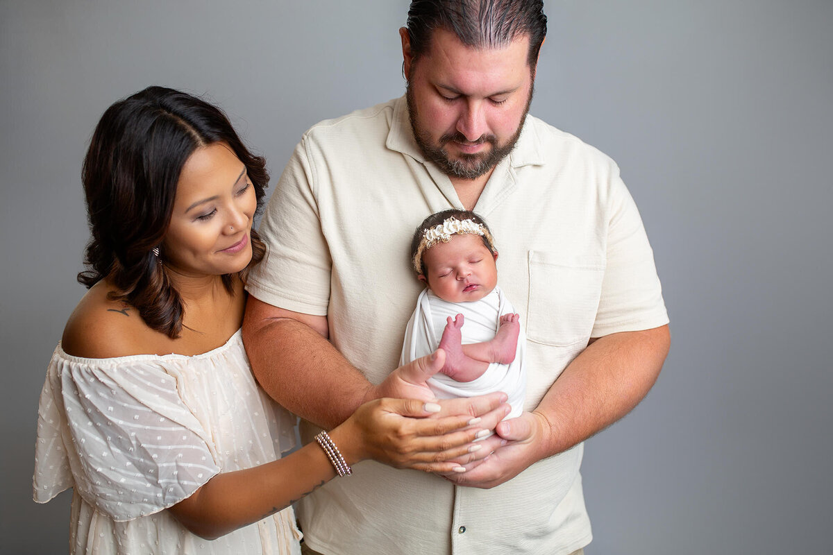 Studio family portrait of father holding the baby and mother snuggling on dad and baby 