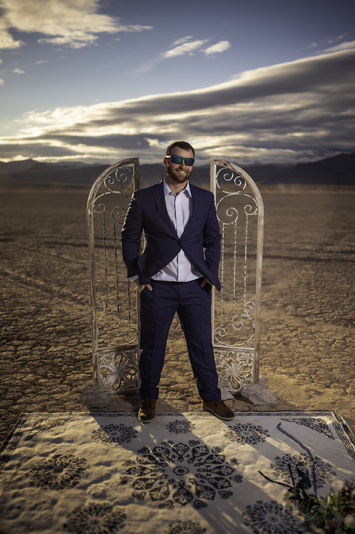 oakley mens straight-backed sunglasses blue suit Dry lake Bed elopement Blue Suit on Groom  flowers by michelle  bride in cream color wedding dress with deep  plunging  neckline mountain skyline  sunset las vegas wedding photographers mk delacy photography