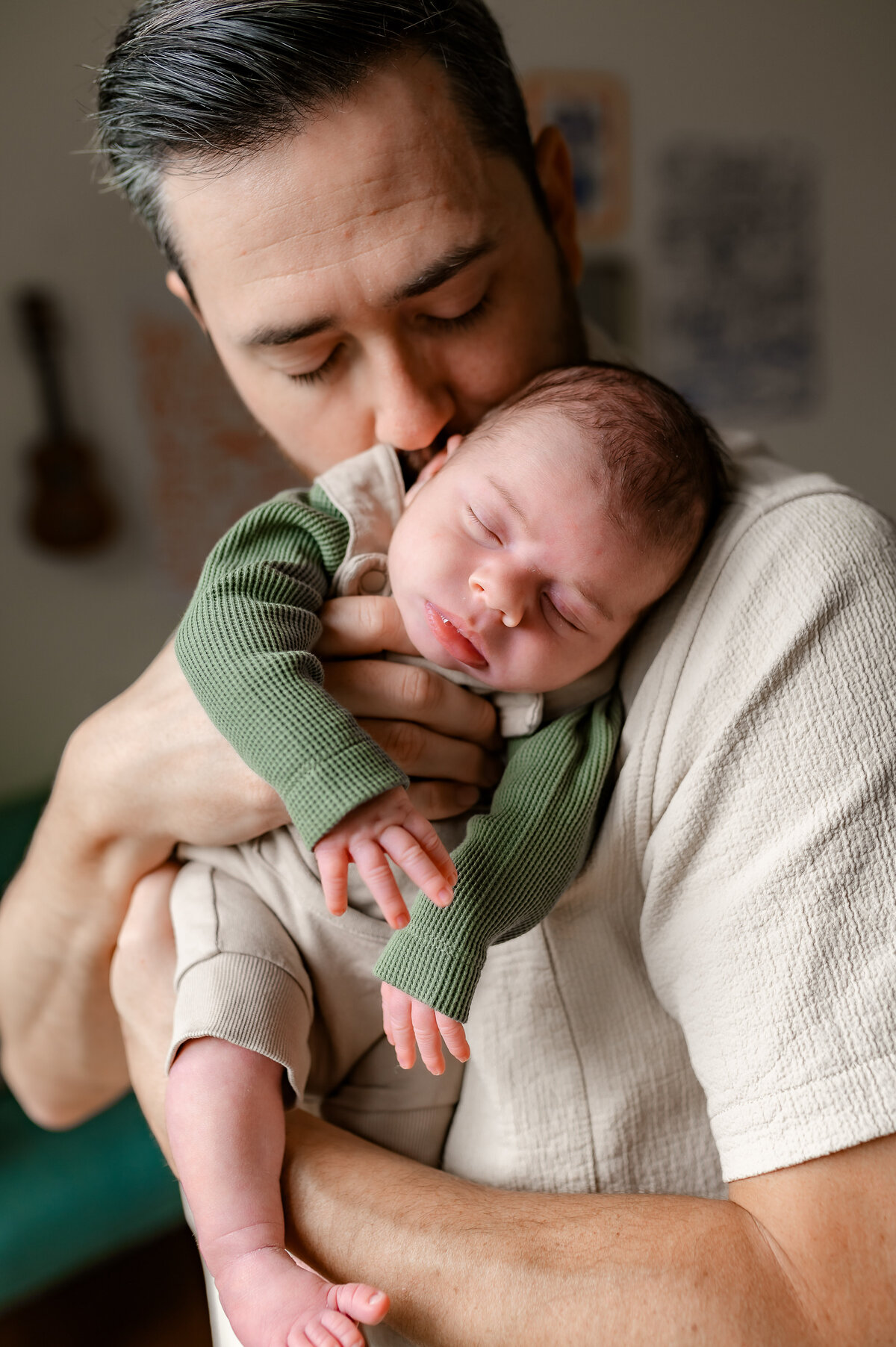 A father holds his newborn against his chest, wrapped in a romper, showcasing a tender, emotional connection.