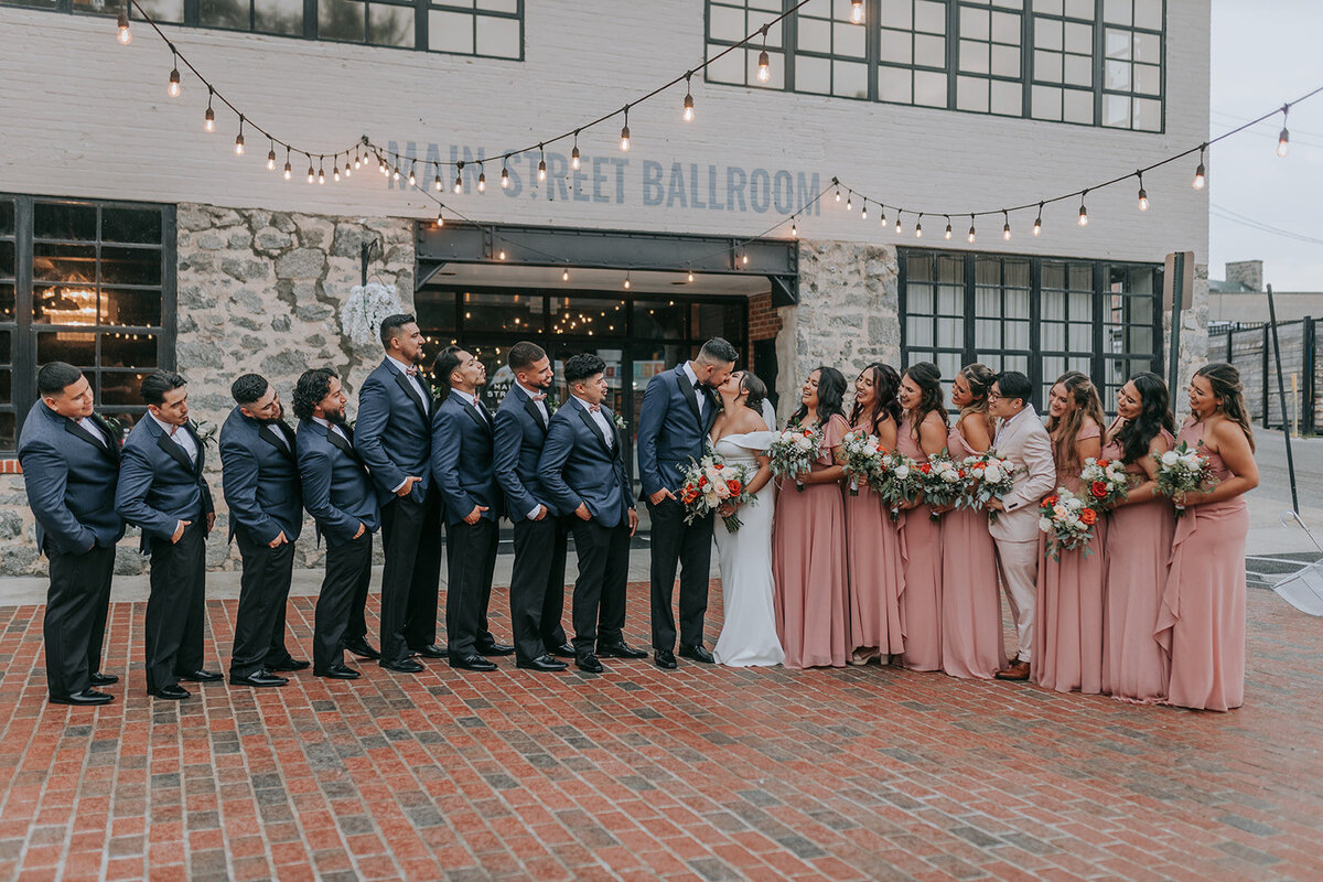 Couples kiss with their wedding parties in the sides