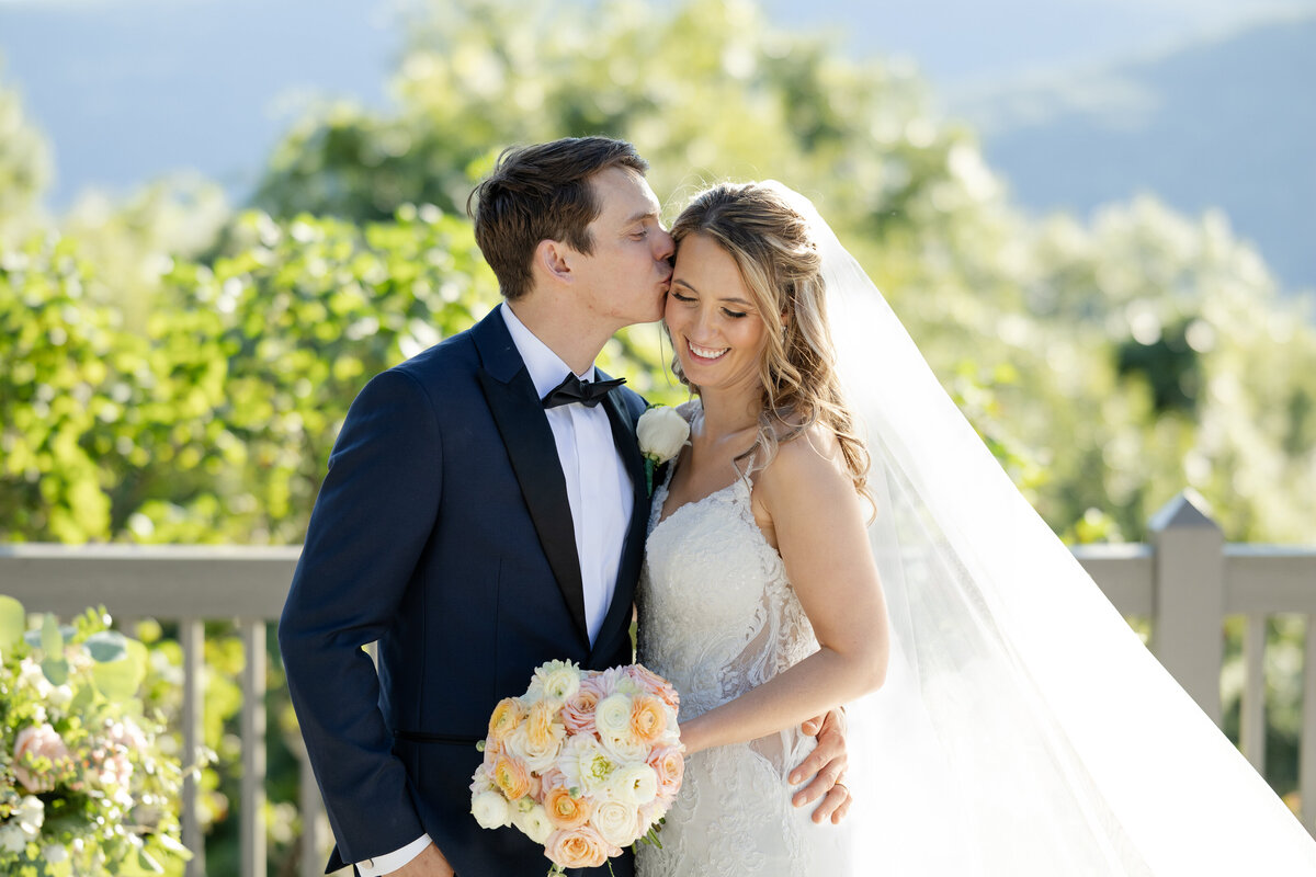 Groom kisses the side of his bride's temple, with the Catskill Mountains behind them 