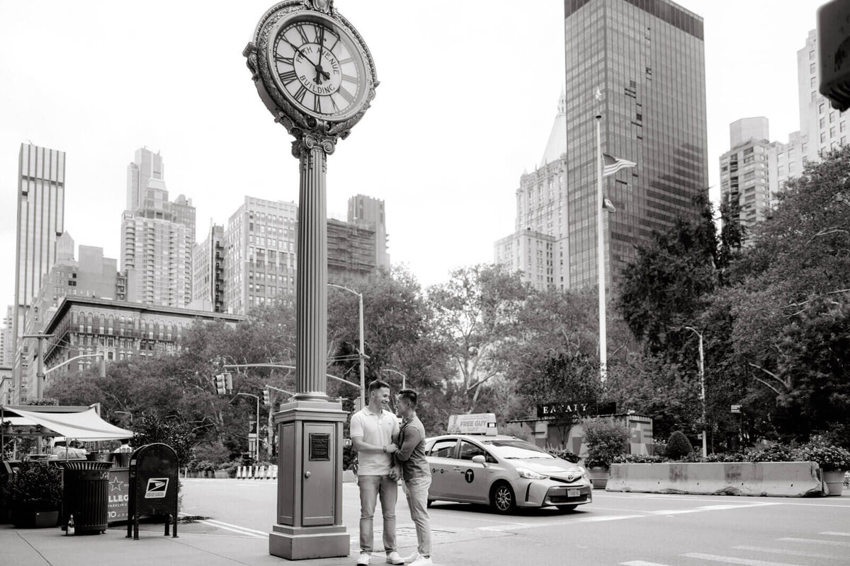 The engaged couple is standing beside a sidewalk clock in West Village, NYC. Image by Jenny Fu Studio.
