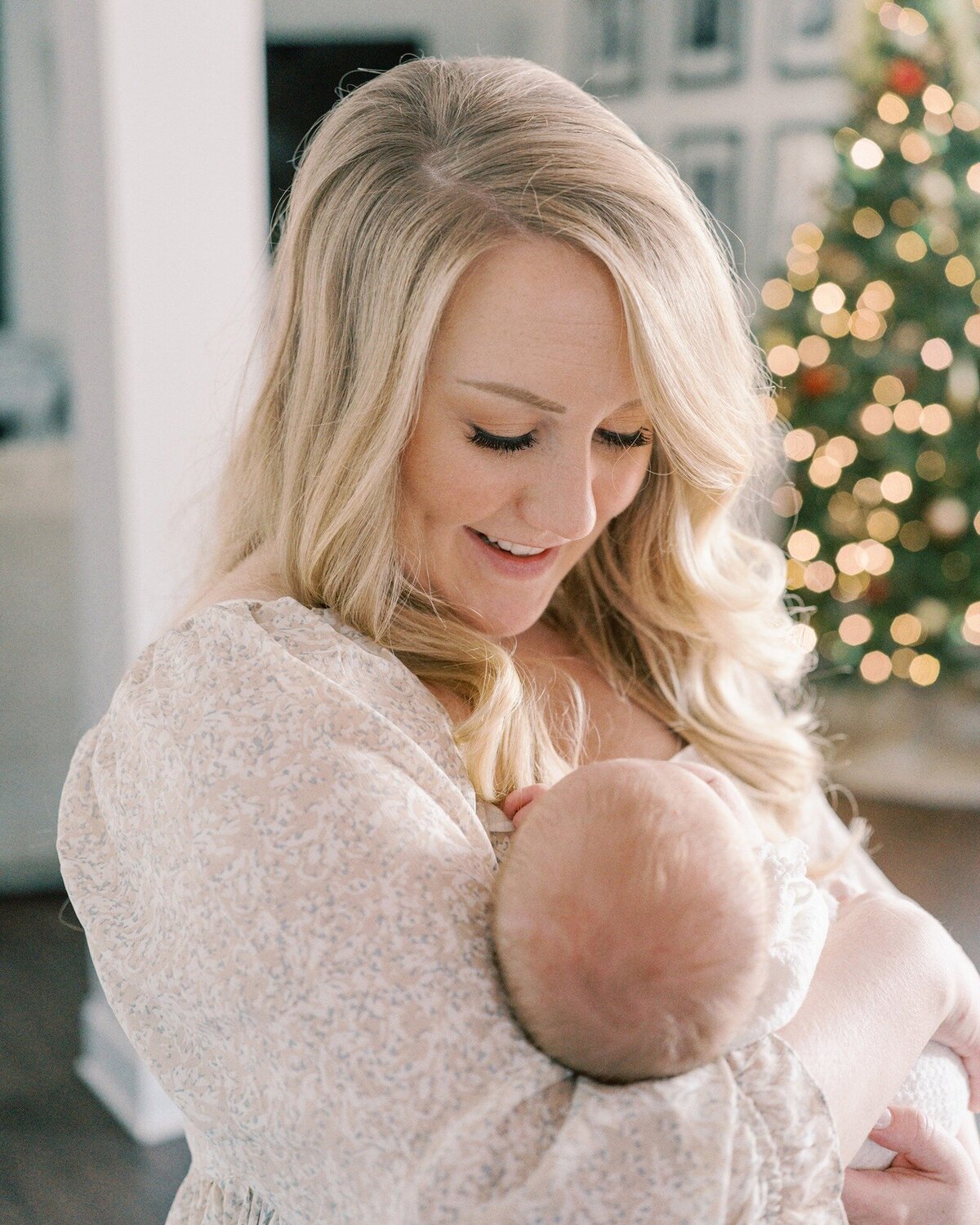 young-mom-holding-newborn-in-front-of-christmas-tree-bokeh