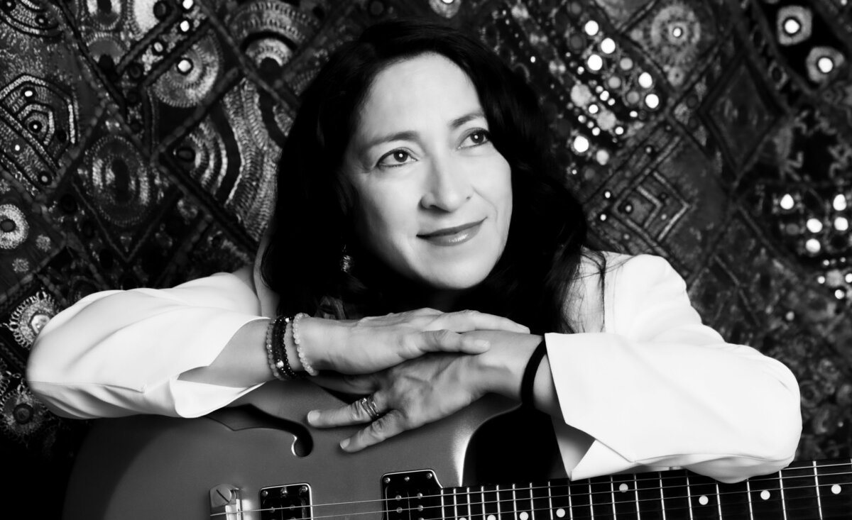 Female musician portrait black and white Rebecca Vest wearing suit with arms leaning atop electric guitar with patterned backdrop