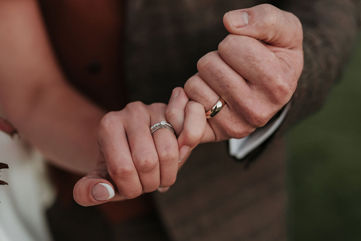 Close up of hands holding a pinky promise to show their wedding rings at a beautiful rustic wedding at Montague Farm, Sussex