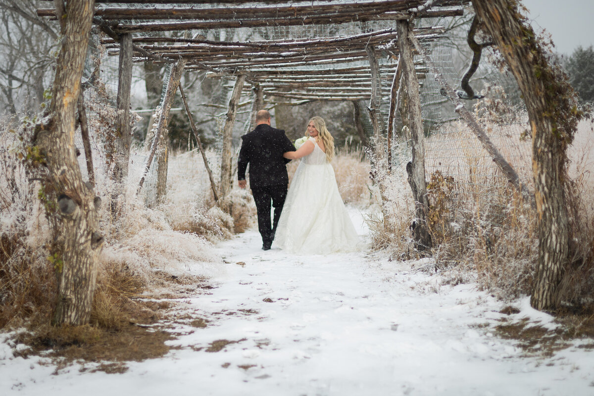Bride looking back as she is escorted by her groom down a snow path