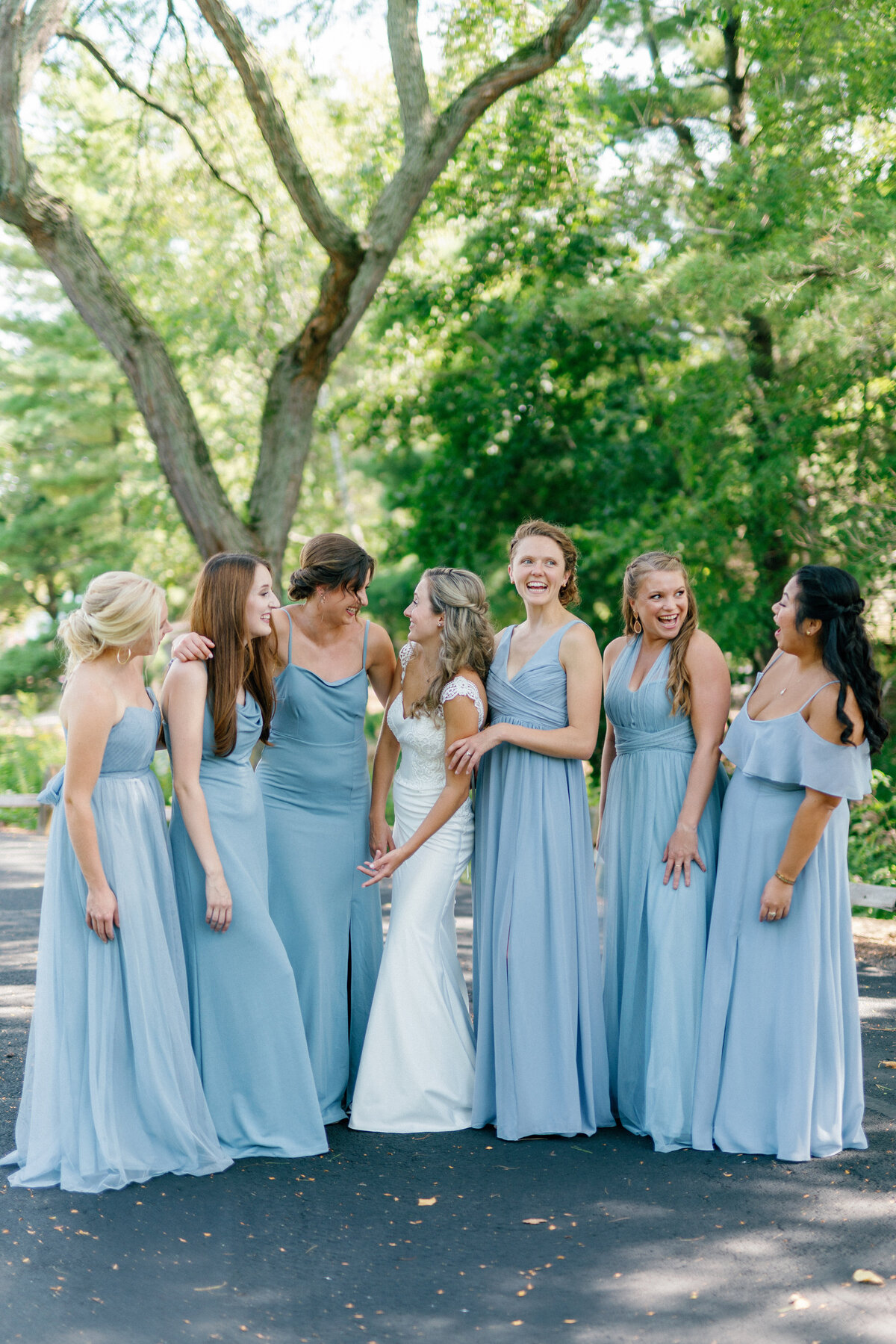 Bride and bridesmaids in  blue dresses laugh in stunning summer wedding portrait by Illinois wedding photographer Lacey Graham