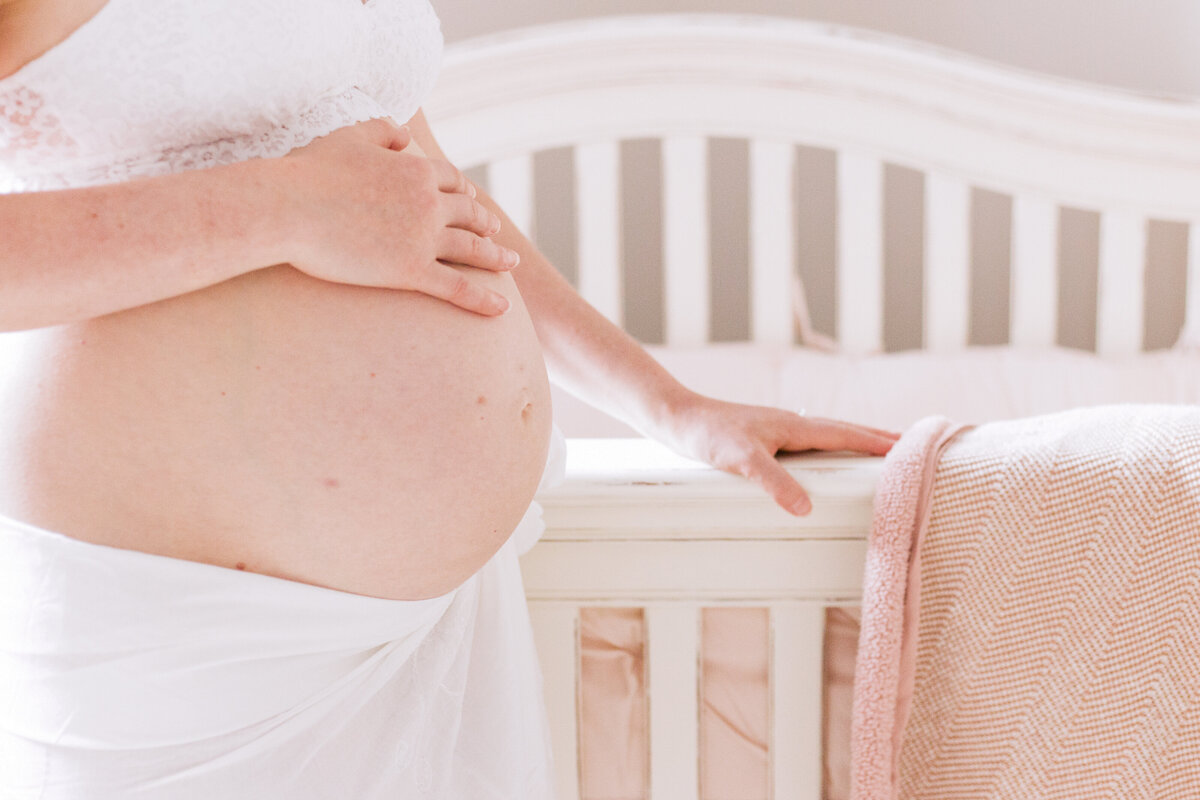 pregnant belly next to white baby crib