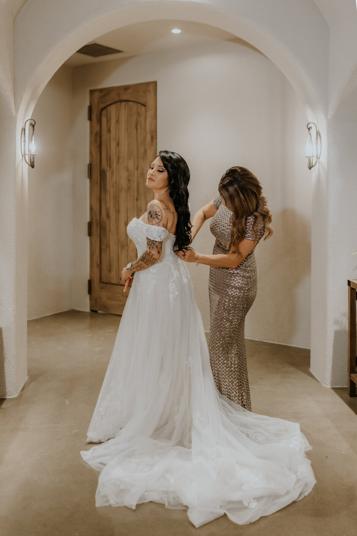 Lady helps bride zip up wedding dress